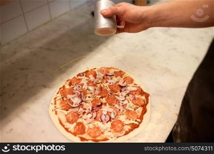 food, culinary, italian cuisine, people and cooking concept - cook hand adding pepper to salami pizza at pizzeria. cook adding pepper to salami pizza at pizzeria