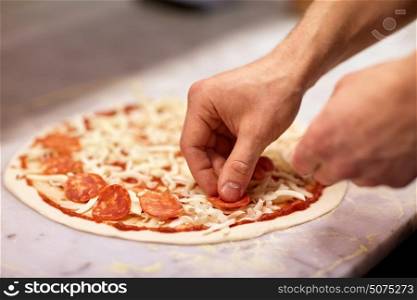 food, culinary, italian cuisine, people and cooking concept - cook hands adding salami slices to pizza at pizzeria. cook hands adding salami to pizza at pizzeria