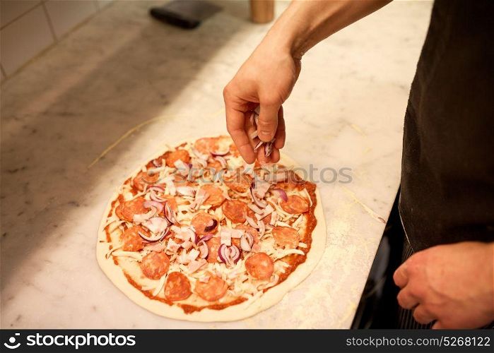 food, culinary, italian cuisine, people and cooking concept - cook hands adding red onion to salami pizza at pizzeria. cook adding onion to salami pizza at pizzeria
