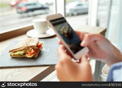 food, culinary, technology and people concept - woman hands with smartphone photographing panini sandwich at restaurant