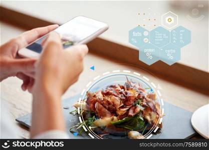 food, culinary, technology and people concept - woman hands with smartphone, prosciutto ham salad on stone plate and nutritional value chart at restaurant. hands with phone and food nutritional value chart