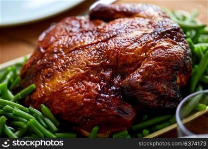 food, culinary, thanksgiving day and eating concept - close up of roast or grilled chicken with garnish of green beans on table. close up of roast chicken with green beans