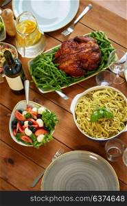 food, culinary, thanksgiving day and eating concept - pasta with basil, vegetable salad and roast chicken on wooden table. pasta, vegetable salad and roast chicken on table