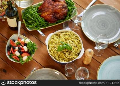 food, culinary, thanksgiving day and eating concept - pasta with basil, vegetable salad in bowl and roast chicken on wooden table. pasta, vegetable salad and other food on table