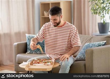 food delivery, consumption and people concept - happy man eating takeaway pizza at home. happy man eating takeaway pizza at home