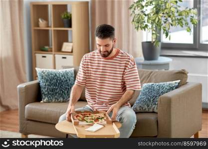 food delivery, consumption and people concept - happy man opening box and eating takeaway pizza at home. man opening box and eating takeaway pizza