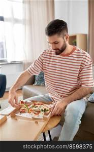 food delivery, consumption and people concept - happy man opening box and eating takeaway pizza at home. man opening box and eating takeaway pizza