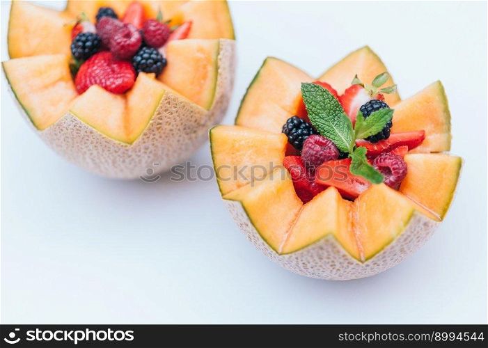Food design and healthy nutrition concept. Delisious fresh raspberry, strawberry and blackberry with mint in carved melon. Cantaloupe with fruit against white background.