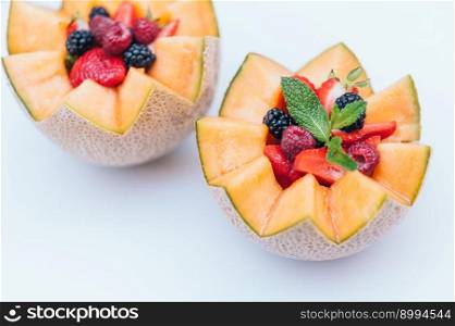 Food design and healthy nutrition concept. Delisious fresh raspberry, strawberry and blackberry with mint in carved melon. Cantaloupe with fruit against white background.