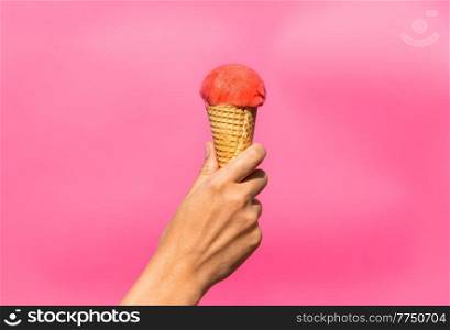 food, dessert and eating concept - close up of hand holding ice cream in waffle cone over pink background. close up of hand holding waffle ice cream cone