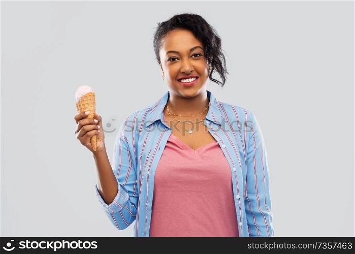 food, dessert and eating concept - happy african american young woman with ice cream cone over grey background. happy african american woman with ice cream cone