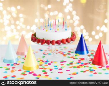 food, dessert and party concept - birthday cake with candles and strawberries on stand over lights on beige background. birthday cake with candles and strawberries