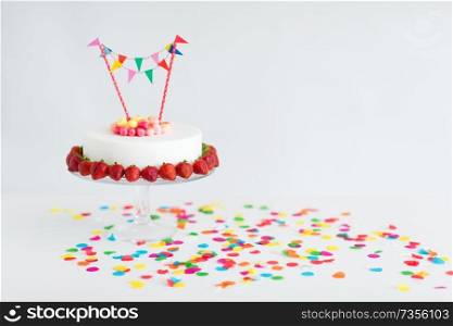 food, dessert and party concept - close up of birthday cake with candies, garland and strawberries on stand. close up of birthday cake with garland on stand