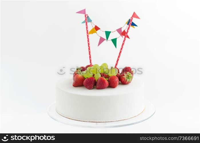 food, dessert and party concept - close up of birthday cake with garland, strawberries and grapes on stand. close up of birthday cake with garland on stand