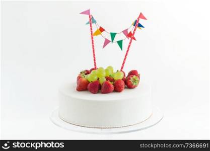 food, dessert and party concept - close up of birthday cake with garland, strawberries and grapes on stand. close up of birthday cake with garland on stand
