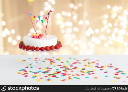 food, dessert and party concept - close up of birthday cake with candies, garland and strawberries on stand over lights on beige background. close up of birthday cake with garland on stand