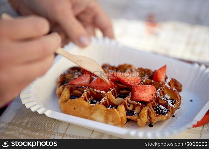 food, dessert and people concept - close up of woman eating waffle with strawberry. close up of woman eating waffle with strawberry