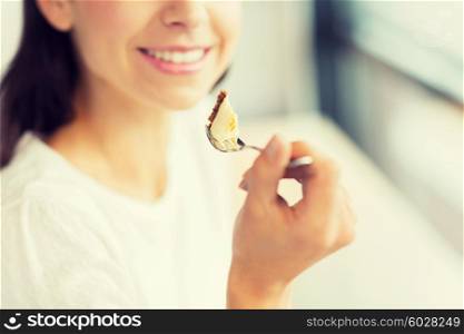 food, dessert, people and lifestyle concept - close up of smiling young woman holding fork and eating cake at cafe or home