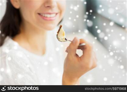 food, dessert, people, holidays and lifestyle concept - close up of smiling young woman holding fork and eating cake at cafe or home over snow effect