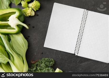 food, diet and healthy eating concept - close up of different green vegetables and diary with empty pages on slate stone background. green vegetables and diary with empty pages