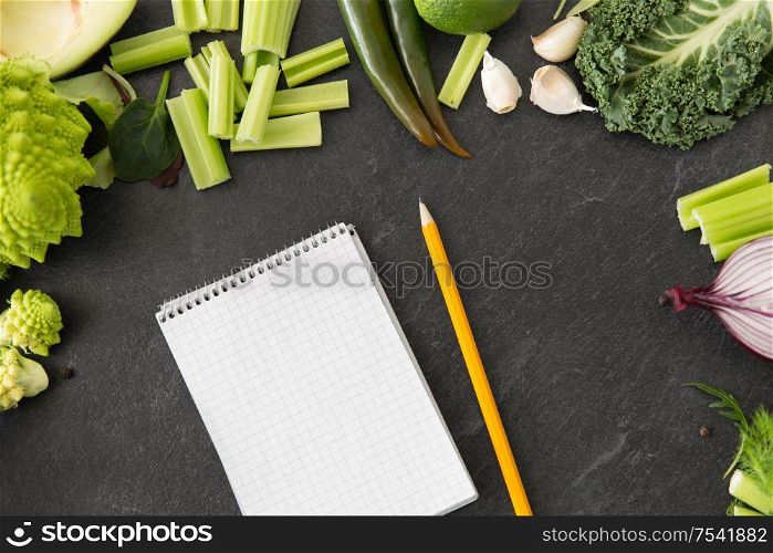 food, diet and healthy eating concept - close up of different green vegetables and diary with empty pages and pencil on slate stone background. green vegetables and diary with empty pages