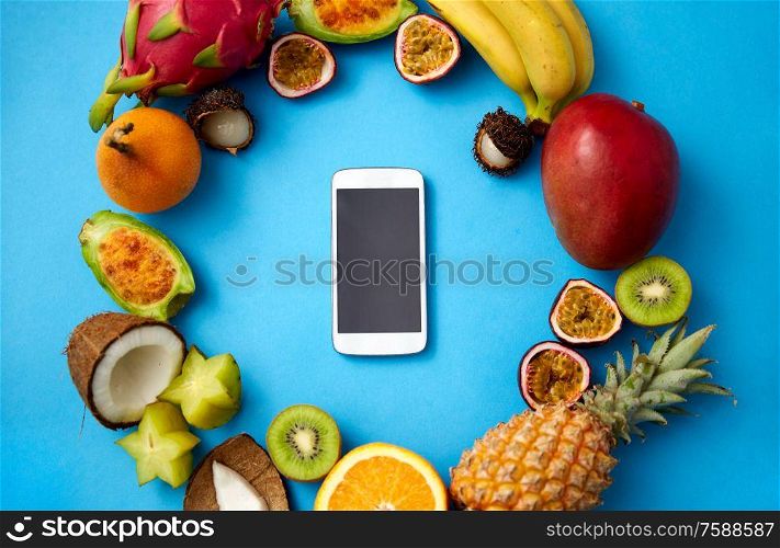 food, diet and healthy eating concept - different exotic fruits around smartphone on blue background. exotic fruits around smartphone on blue background