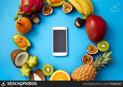 food, diet and healthy eating concept - different exotic fruits around smartphone on blue background. exotic fruits around smartphone on blue background