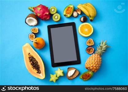 food, diet and healthy eating concept - different exotic fruits around tablet pc computer on blue background. fruits around tablet computer on blue background