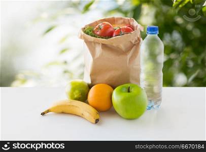 food, diet and healthy eating concept - paper bag with fresh fruits and vegetables and water bottle on table over green natural background. paper bag with vegetable food and water on table. paper bag with vegetable food and water on table