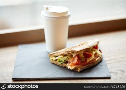 food, dinner and eating concept - salmon panini sandwich with tomatoes and cheese on stone plate and cup of drink on cafe table