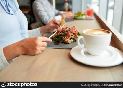 food, dinner and people concept - woman eating prosciutto ham salad on stone plate at restaurant and coffee cup on table