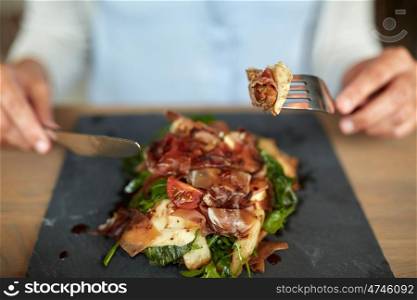 food, dinner and people concept - woman eating prosciutto ham salad on stone plate at restaurant
