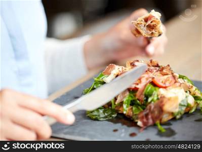 food, dinner and people concept - woman eating prosciutto ham salad on stone plate at restaurant