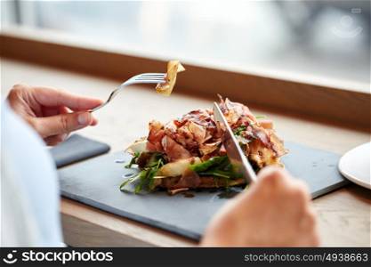 food, dinner and people concept - woman eating prosciutto ham salad on stone plate at restaurant. woman eating prosciutto ham salad at restaurant