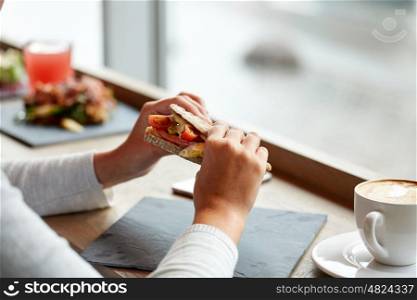 food, dinner and people concept - woman eating salmon panini sandwich with tomatoes and cheese at restaurant