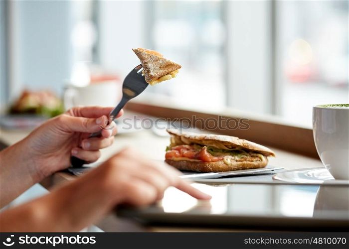 food, dinner and people concept - woman with tablet pc computer eating salmon panini sandwich at restaurant