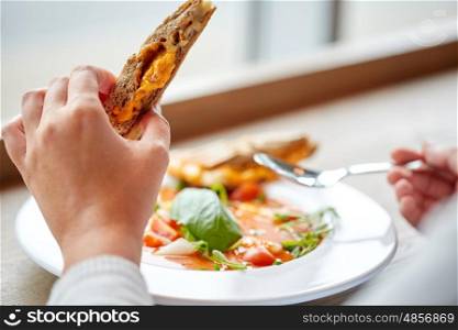 food, dinner, culinary and people concept - close up of woman eating gazpacho soup with sandwich and spoon at restaurant