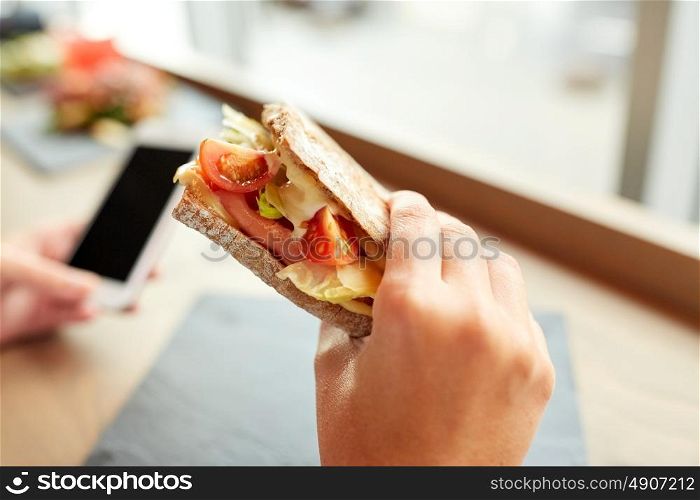food, dinner, eating and people concept - hand with salmon panini sandwich with tomatoes and cheese at restaurant. hand with salmon panini sandwich at restaurant