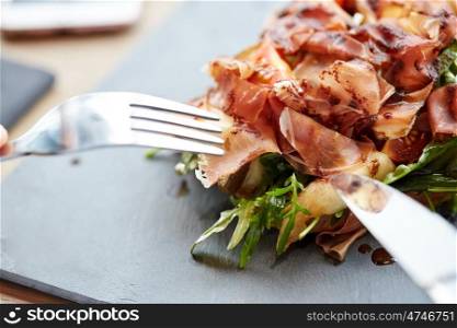 food, dinner, haute cuisine and eating concept - close up of prosciutto ham salad on stone plate at restaurant
