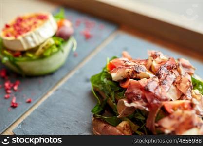 food, dinner, haute cuisine and eating concept - prosciutto ham and cheese salads on stone plates at restaurant