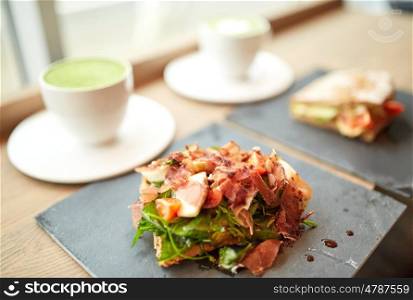 food, dinner, haute cuisine and eating concept - prosciutto ham salad on stone plate with matcha green tea latte and sandwich at restaurant
