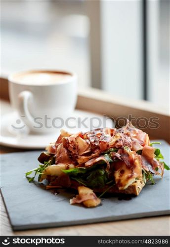 food, dinner, haute cuisine and eating concept - prosciutto ham salad on stone plate and coffee cup at restaurant