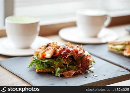 food, dinner, haute cuisine and eating concept - prosciutto ham salad on stone plate and coffee cups at restaurant