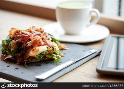 food, dinner, haute cuisine and eating concept - prosciutto ham salad on stone plate with tablet pc and drink at restaurant