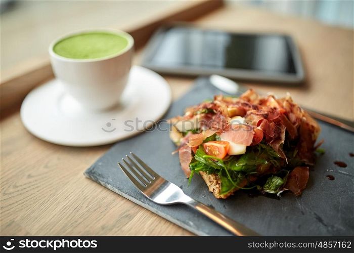 food, dinner, haute cuisine and eating concept - prosciutto ham salad on stone plate with matcha green tea latte and tablet pc computer at restaurant