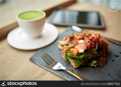 food, dinner, haute cuisine and eating concept - prosciutto ham salad on stone plate with matcha green tea latte and tablet pc computer at restaurant