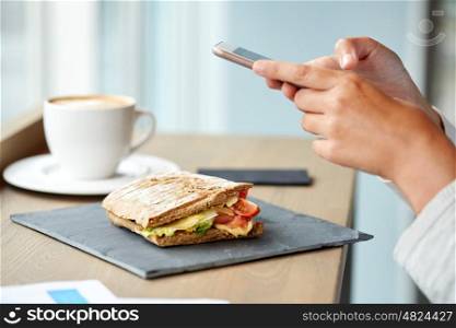 food, dinner, technology and eating concept - salmon panini sandwich and woman with smartphone on stone plate at cafe
