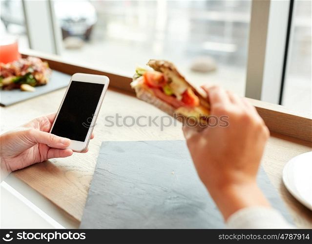 food, dinner, technology and people concept - woman with smartphone eating salmon panini sandwich with tomatoes and cheese at restaurant