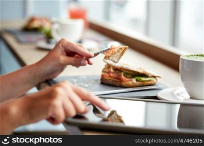 food, dinner, technology and people concept - woman with tablet pc computer eating salmon panini sandwich at restaurant