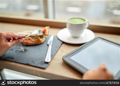 food, dinner, technology and people concept - woman with tablet pc computer and matcha green tea latte eating salmon panini sandwich at restaurant